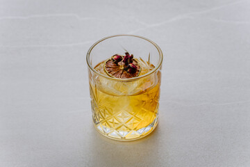 Elegant whiskey cocktail with dried lime and rosebuds in faceted glass on light background
