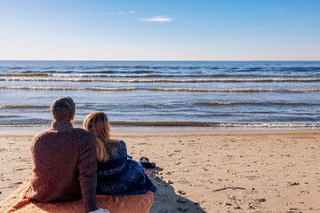 Loving couple walks on beach along sea on sunny autumn day. Weekend and lifestyle concept. Back view. High quality photo