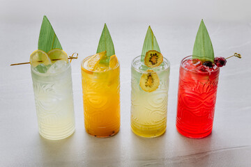 Tropical colorful cocktails in tiki glasses with ice and exotic fruit garnish on light background