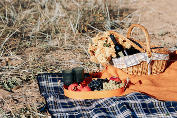 Autumn picnic on beach by sea. Fresh fruits, wine glasses, bottle, grapes, pomegranate near picnic basket on orange blanket. High quality photo