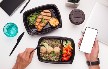 Man eating healthy food preparing on grill on workplace and holding cellphone with blank space