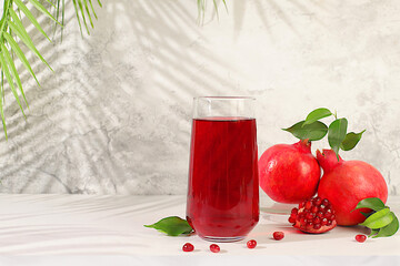 Modern still life with pomegranate juice and grains with ripe pomegranates on a fashionable table in the shade of palm trees, conceptual holiday party, bar and cafe advertising.