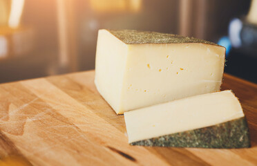 Hard cheese pieces on wooden table at grocery shop background. Gruyere in herbs shell, closeup