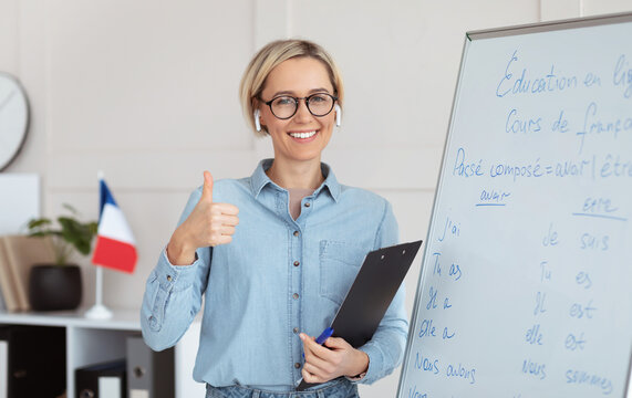 Friendly female teacher recommending foreign languages school, showing thumb up gesture, giving French lesson. Positive young tutor satisfied with educational services