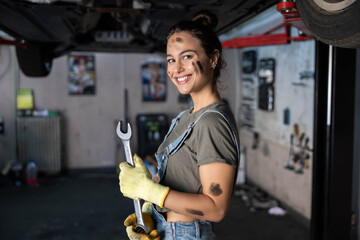 A mechanic confidently poses with wrenches in a garage, symbolizing strength and skill in the field of automotive work.