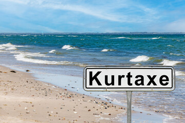 Kurtaxe sign on sandy beach with ocean waves crashing