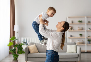 Fototapeta premium Laughing young mother playing with cute toddler son, holding funny kid pretending flying, loving happy mum lifting child boy, having fun together at home