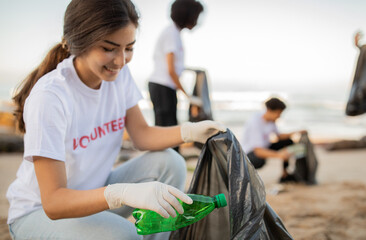 Glad young people volunteers and asian lady in gloves with garbage bag clean up trash on sea beach, outdoor. Environment conservation, protecting planet, Earth day and ocean pollution