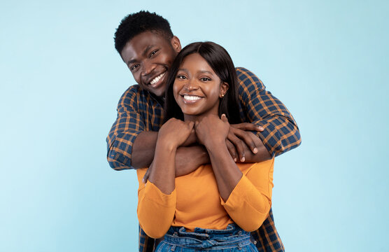 Happy Loving Family. Portrait of cheerful black couple hugging at blue studio background, closeup. Smiling young man embracing his beautiful girlfriend from behind, millennials spending time together