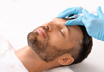 Unrecognizable cosmetologist in protective gloves injecting filler between mans eye brows against...