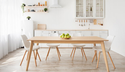 Scandinavian home interior. White and wooden kitchen furniture with various utensils, shelves with plants in pot and dishes, plate with apples on dinning table, panorama