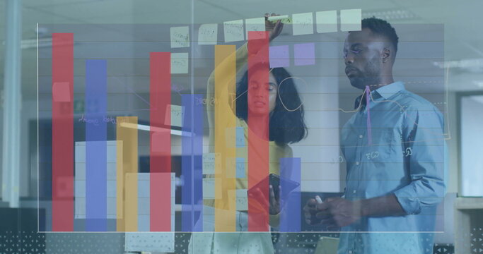 Collaborating colleagues adjusting notes on glass board at office, with smartphone, digital charts - Powered by Adobe