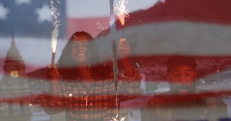 Two friends raising sparklers under translucent US flag overlay at waterfront dusk, plaid shirt