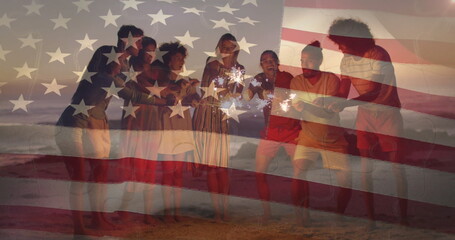 Group of eight friends holding sparklers on sandy beach at dusk, with American flag overlay