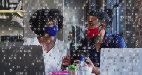 Discussing project two masked colleagues using laptops in cafe, with succulent and binary overlay