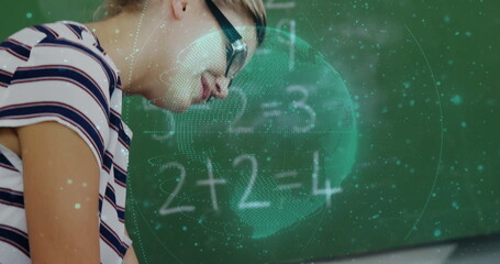 Leaning student with glasses solving math equations at school desk with hologram globe, chalkboard