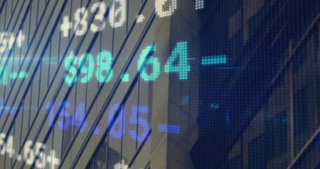 Displaying LED ticker display showing cyan and blue stock prices over office facade, metal mullions