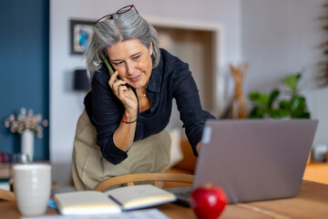 Businesswoman talking on phone and working on laptop at home