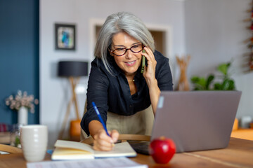 Businesswoman working from home talking on phone and taking notes