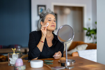 Senior woman applying makeup remover at home using cotton pad