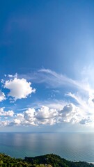 Obraz premium Panoramic view of a bright blue sky with puffy white clouds over a tranquil ocean and distant green hills