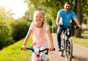 Day in the park. Happy family of caucasian father and girl child riding bicycles outdoors in the...