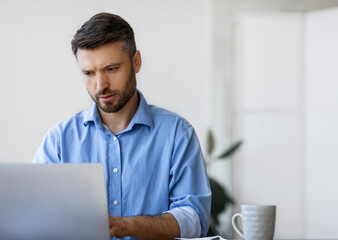Concentrated businessman working on laptop at workplace in office, male entrepreneur looking at...