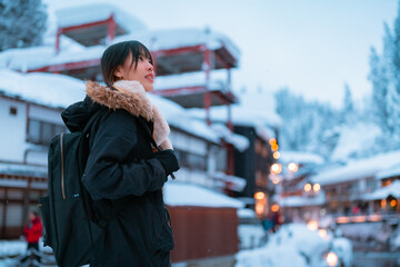 Fototapeta premium Happy Asian woman travel Ginzan Onsen hot spring ryokan area in Yamagata prefecture on winter holiday vacation. Attractive girl looking beautiful nature in snow while travel local village in Japan.