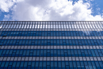 Glass facade of modern office building reflective blue windows showing clouds in sky, urban architecture pattern, business tower exterior, contemporary city design, corporate construction background