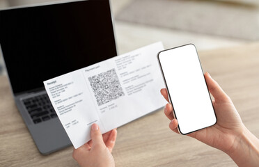 Female hands holding smartphone and scanning the QR code from paper bill, cellphone with white blank screen. Paying online from home, modern technologies concept