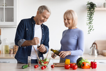 Attractive mature man and woman in casual outfits cooking together at home, making delicious...