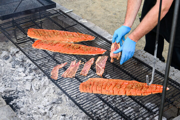 Chef dropping raw Korean style beef onto an outdoor barbeque grill to cook along with teriyaki king...