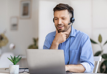 Business Education. Handsome young businessman in headset watching webinar on laptop in modern...