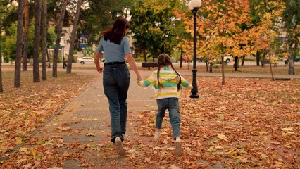 Obraz premium Baby mom play together, run on dry leaves in park holding hands, autumn outdoors. Happy child running holding hands with his mother on yellow autumn leaves. Fun family walk, mom child daughter in park