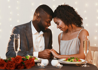 Beautiful african man and woman in love cuddling during valentine dinner, holding hands