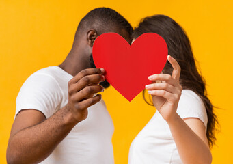 Happy Valentine's Day Concept. Romantic interracial couple kissing behind big red paper heart,...