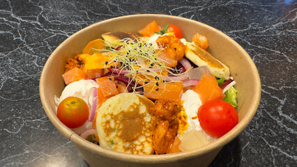 Gourmet salad bowl with smoked salmon, blinis, and fresh cheese on a dark marble background