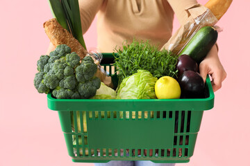 Woman holding green shopping basket with different fresh products on pink background