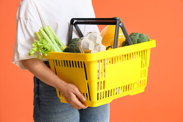 Woman holding yellow shopping basket with different fresh products on orange background