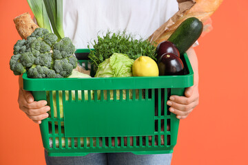Woman holding green shopping basket with different fresh products on orange background