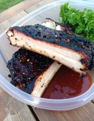 BBQ ribs in a container with sauce and garnish