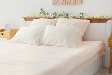 Bed with stylish pink bedding, flowers and bedside tables in bedroom