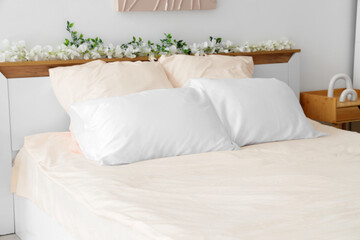 Bed with stylish pink bedding, flowers and bedside table in bedroom