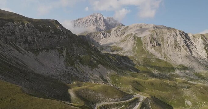 Aerial view of the rugged Gran Sasso mountains, where rocky peaks meet green slopes under a sky with scattered clouds, Gran Sasso, Abruzzo, Italy.