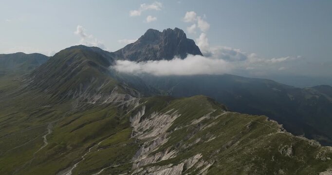 Aerial view of the rugged Gran Sasso mountains, where rocky peaks meet lush green slopes under a serene sky, Gran Sasso, Abruzzo, Italy.