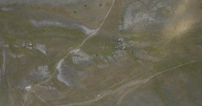 Aerial view of a rugged landscape featuring winding paths amid sparse vegetation and rocky outcrops, creating a textured tableau, Gran Sasso, Abruzzo, Italy.