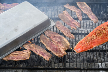 King salmon filets with teriyaki sauce and sesame seeds grilling on an outdoor barbeque pit, along...