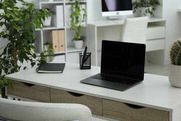 Stylish workplace with laptop, stationery and floral decor in office. Biophilic interior design
