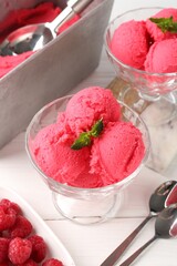 Delicious raspberry sorbet with mint in dessert bowls, spoons and fresh berries on white wooden...