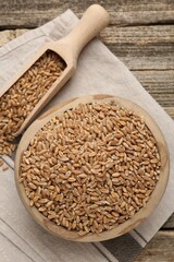 Wheat grains in bowl and scoop on wooden table, flat lay